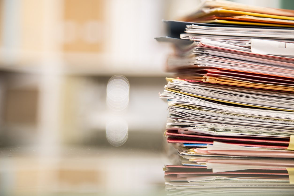 Large stack of files, documents, paperwork on desk. DataBank