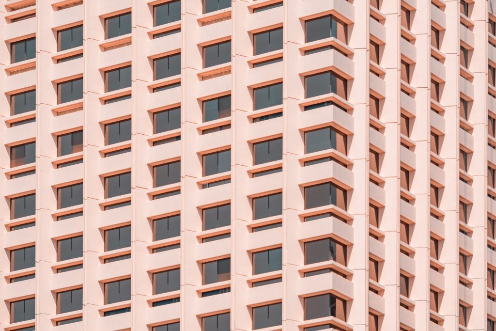 Corner of a tall pink or beige building with many structured windows