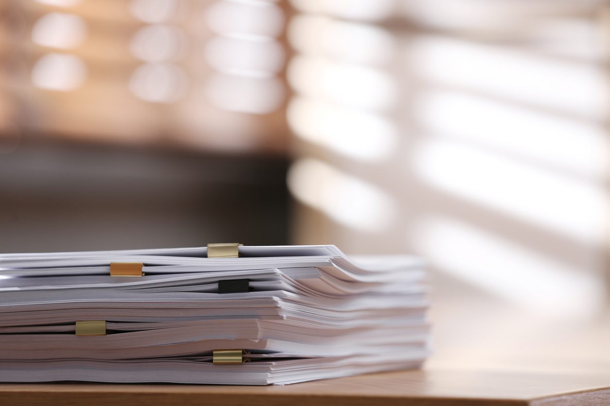 Stack of blank paper with binder clips on wooden table indoors. 